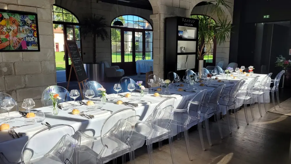 Salle du restaurant Le Preti dressée pour un mariage, avec de longues tables et des chaises habillées de blanc